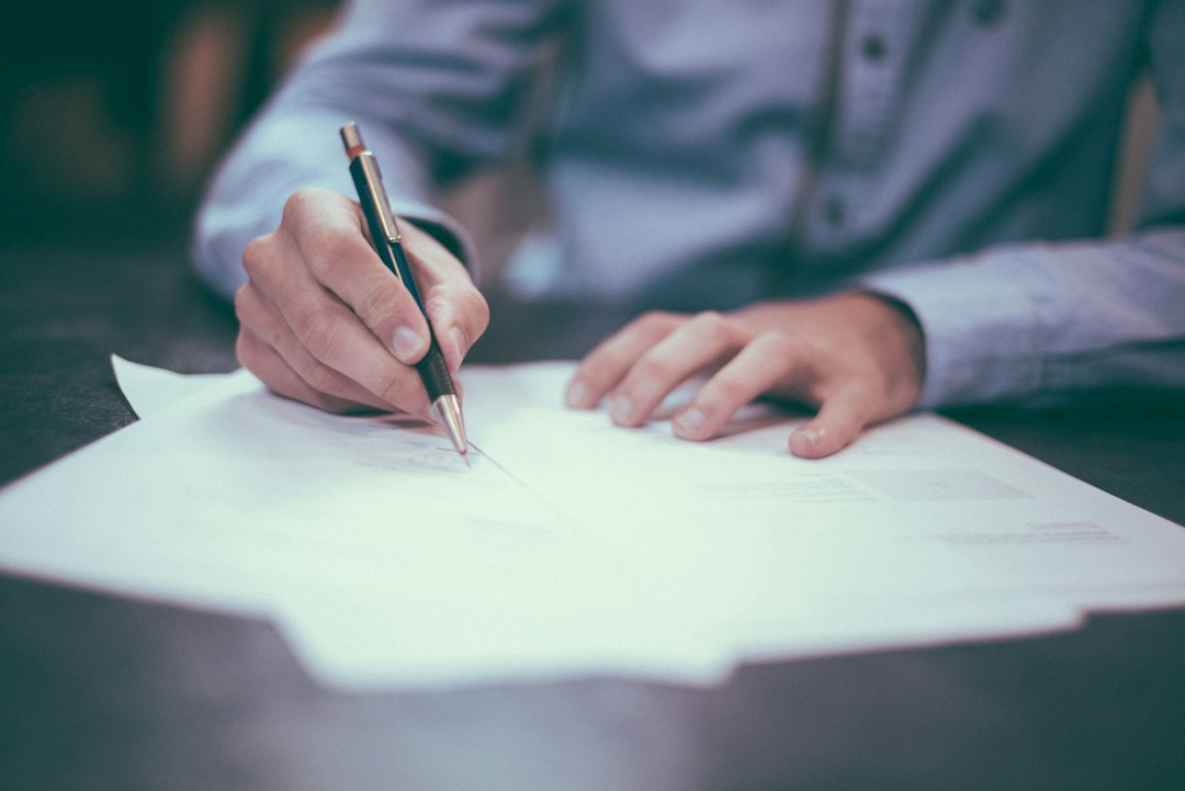 Profissional revisa e assina documento de prestação de serviços; foto de Scott Graham via Unsplash